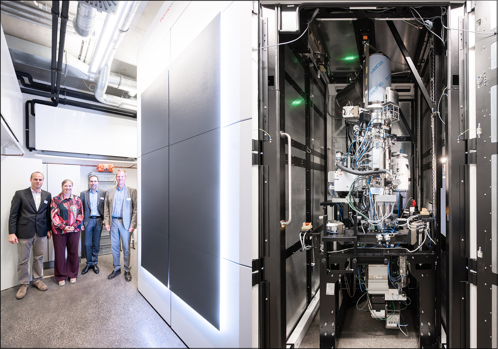 Four scientists standing next to a high-tech scientific instrument and its internal machinery.