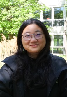 Person vor hellgrüner Gartenlandschaft; Gesicht von Pixeln überdeckt, schwarze Haare, dunkle Jacke.